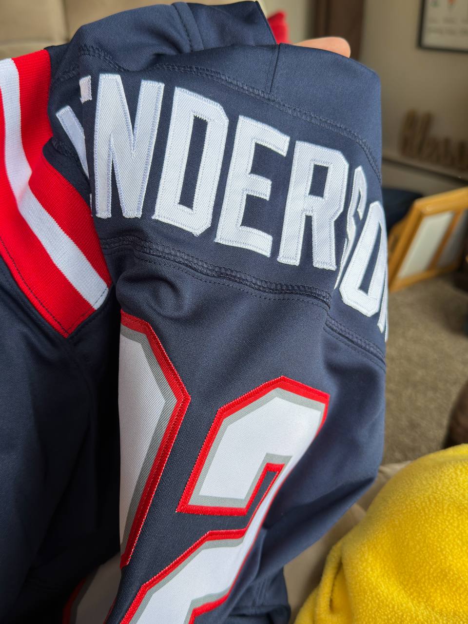 Close-up of the stitched name and number on the back of a navy football jersey with red and white shoulder stripes